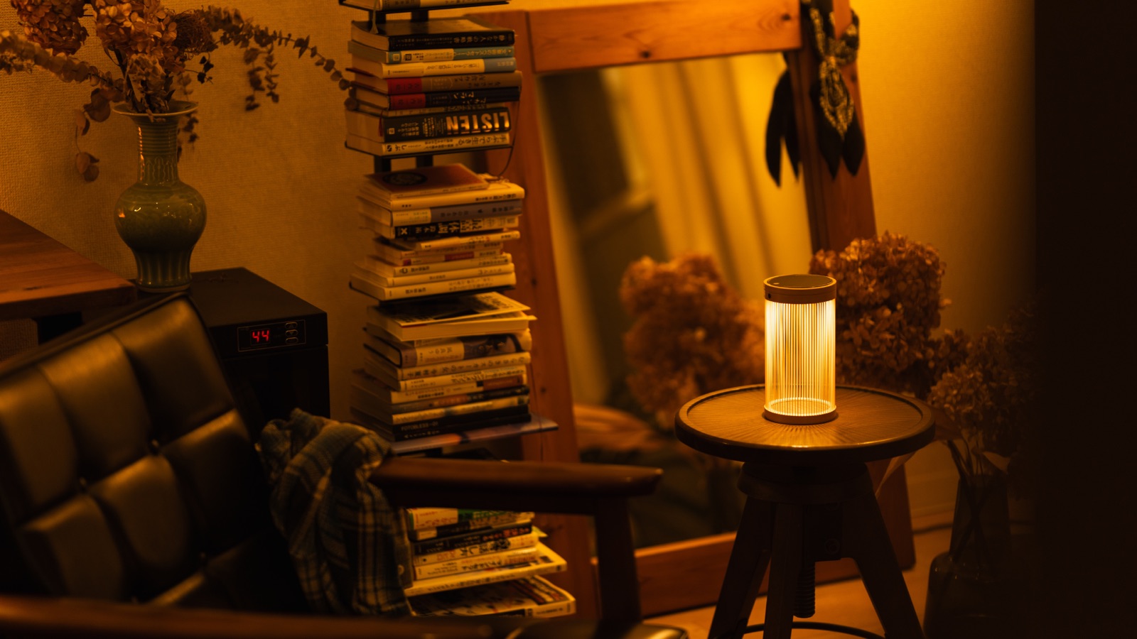 The Sonnenglas® EN (縁) lantern glowing on a small wooden side table, next to a stack of books and a leather armchair