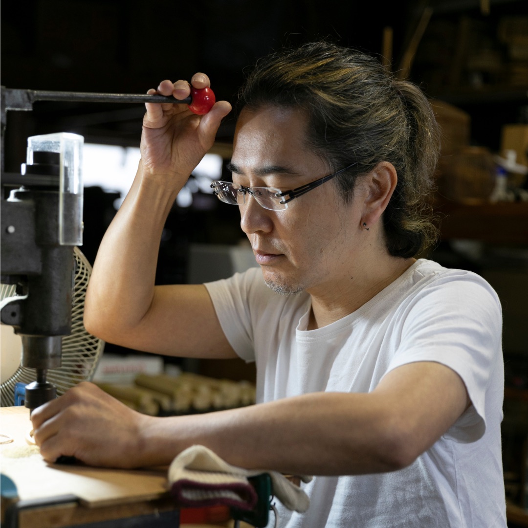 A craftsman with glasses works at a hand press at his workbench
