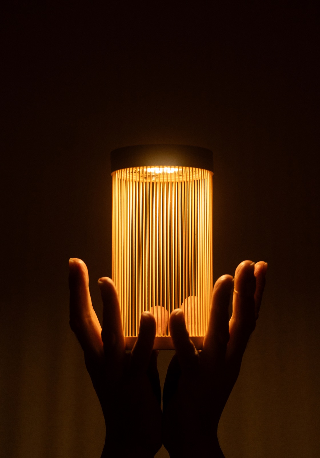 Two hands hold up the glowing Sonnenglas® EN (縁) bamboo lantern in the dark