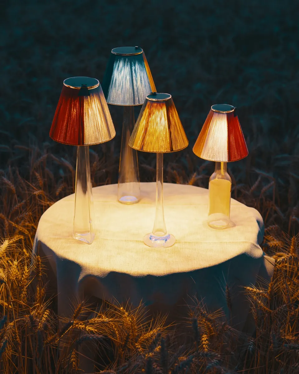 Vier Lightshades mit von Hand gewickelten Baumwollschirmen leuchten auf einem Tisch im Weizenfeld in der Dämmerung