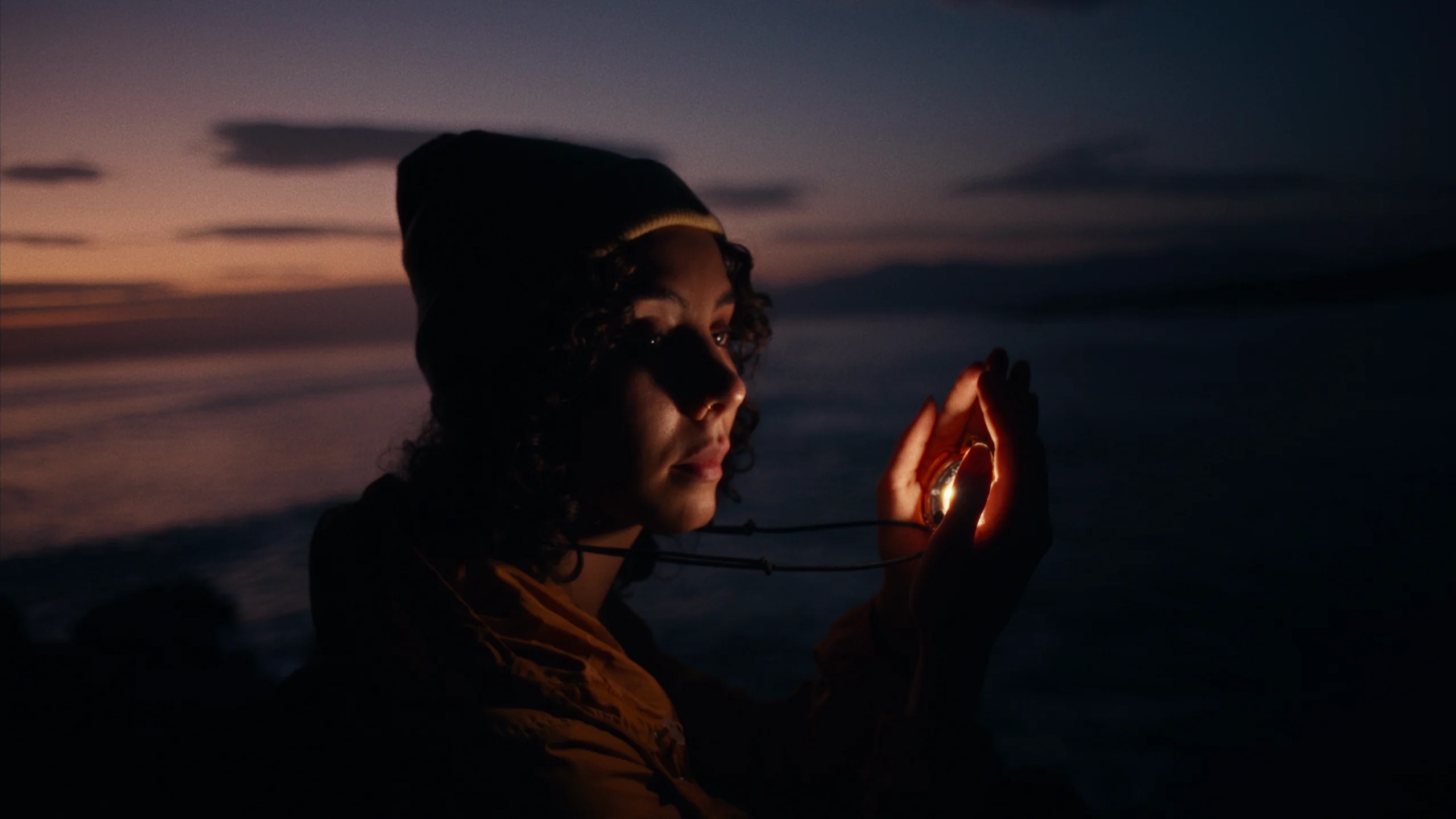 A woman holds a glowing SOMO in her hands at dusk by the sea